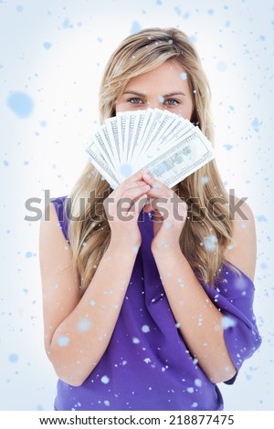 Composite image of Blonde woman hiding her face behind a fan of notes with snow falling