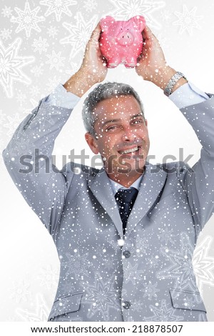 Composite image of Cheerful businessman holding piggy bank above his head with snowflakes on silver