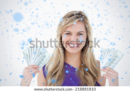 Happy blonde woman holding two fans of notes against snow falling