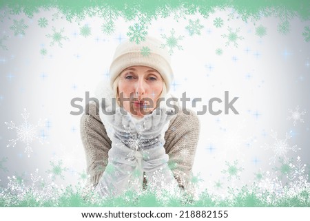 Mature woman in winter clothes blowing kiss against snow flake frame in green