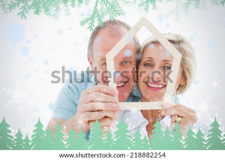 Happy older couple holding house shape against frost and fir trees in green