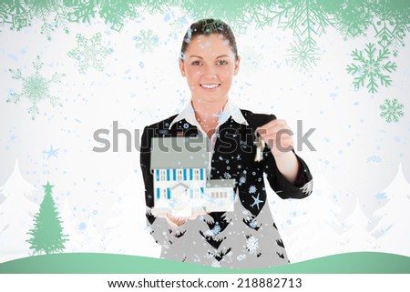 Good looking woman in suit holding keys and a miniature house against snowflakes and fir tree in green