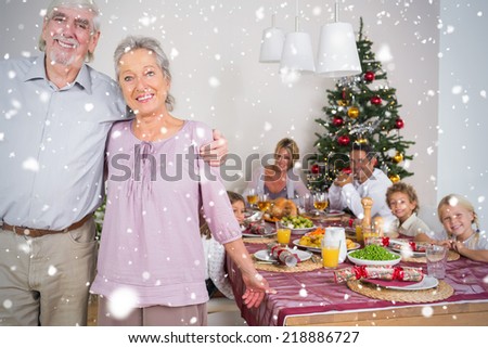 Composite image of Grandparents standing by the dinner table against snow falling