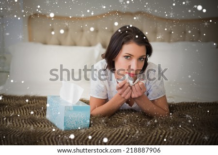 Composite image of calm pretty brown haired woman sneezing in a tissue against snow