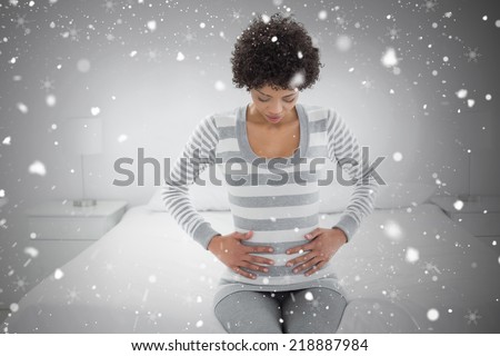 Casual woman with stomach pain sitting in bed against snow falling
