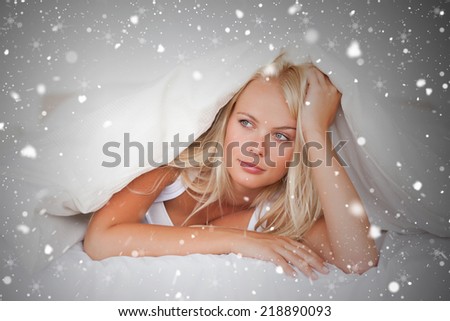 Composite image of woman under a duvet against snow falling