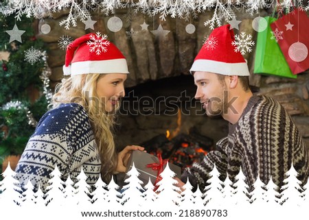 Man gifting woman in front of lit fireplace during Christmas against fir tree forest and snowflakes