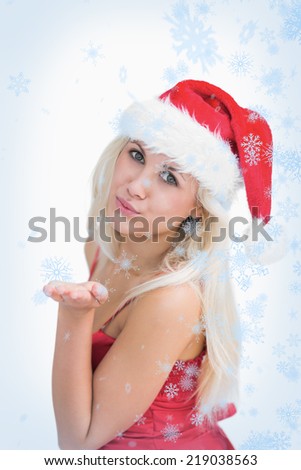 Woman wearing santa hat as she blows kiss against snow falling
