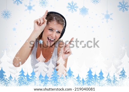 Woman dancing while listening to music against snowflakes and fir trees
