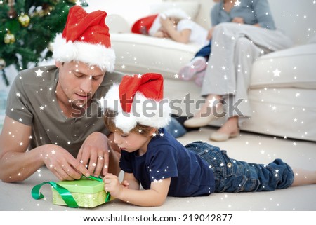 Father and son unwrapping a present lying on the floor against snow