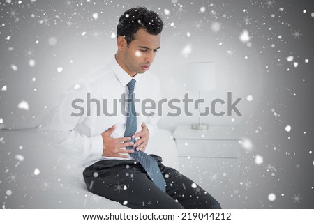 Composite image of businessman with stomach pain sitting on bed against snow falling