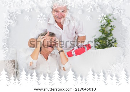 Old man hiding eyes of his wife for a gift against fir tree forest and snowflakes