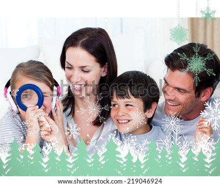 Happy family playing with a magnifying glass against snowflakes and fir trees in green