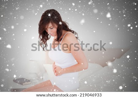 Attractive brunette woman having a stomach ache while sitting against snow falling