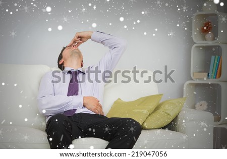 Tired businessman sitting on sofa in living room against snow