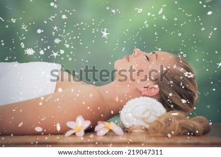 Peaceful blonde lying on bamboo mat with flowers against snow falling