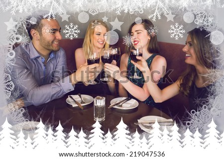 Laughing friends sitting together clinking glasses against fir tree forest and snowflakes