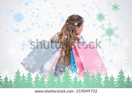Back view of a woman holding shopping bags against snowflakes and fir trees in green