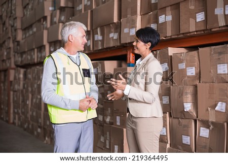 Pretty warehouse manager talking to foreman in a large warehouse