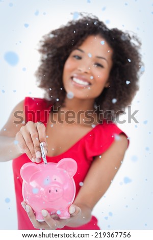 Composite image of Money been put into a pink piggy bank with snow falling