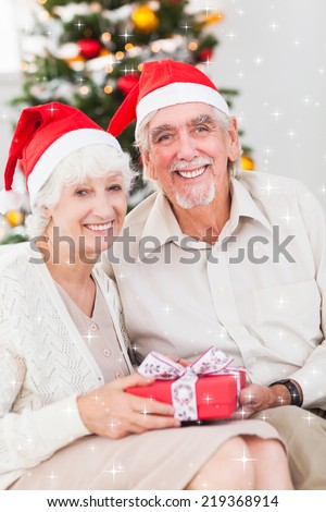 Smiling old couple swapping christmas gifts against twinkling stars