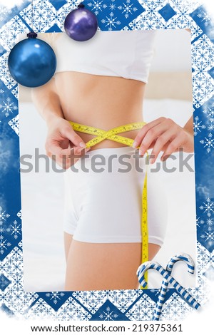 Toned woman measuring her waist against christmas frame
