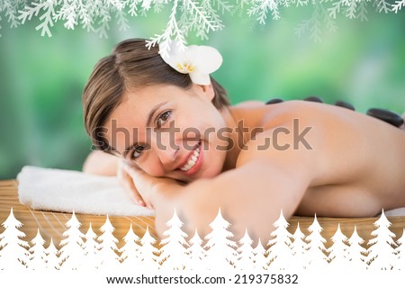 Beautiful woman receiving stone massage at health farm against fir tree forest and snowflakes