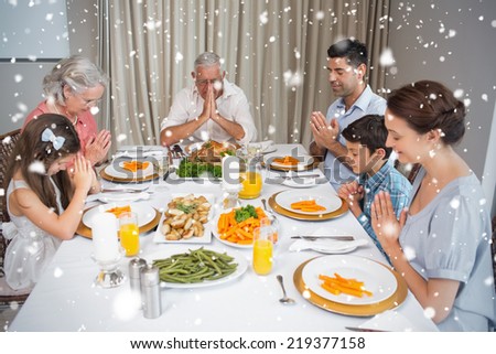 Family of six saying grace before meal at dining table against snow falling