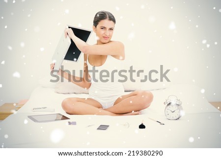 Furious young brown haired model in white pajamas throwing her laptop against snow falling