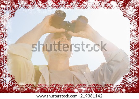 Happy hiker looking through binoculars against snow