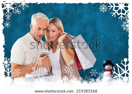 Happy couple with shopping bags and smartphone against christmas themed snow flake frame
