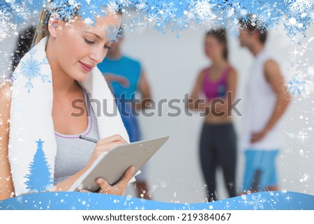 Trainer writing on clipboard with fitness class in background at gym against snow