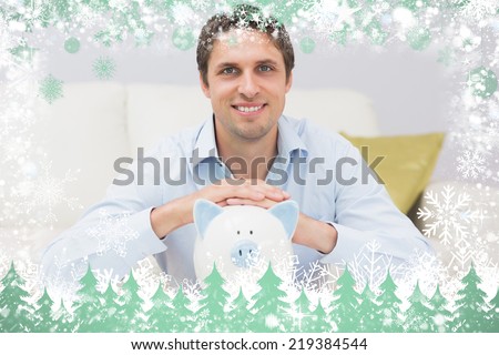 Handsome casual man with piggy bank in living room against snow