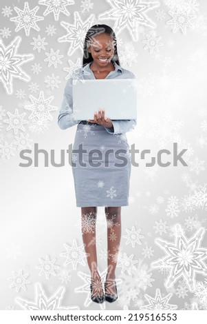 Composite image of Portrait of a smiling businesswoman using a laptop while standing up with snowflakes on silver