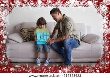 Father and son with gift box sitting in living room against snow