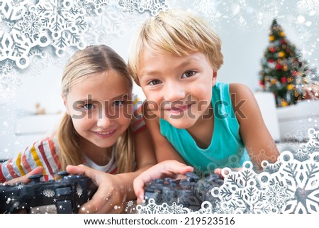 Composite image of happy siblings playing video games on floor against snow