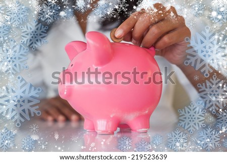 Businesswoman putting coins into pink piggy bank at her desk against snow