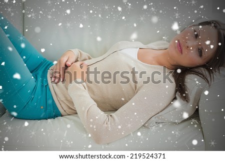 Composite image of anxious and sick woman lying on sofa against snow falling