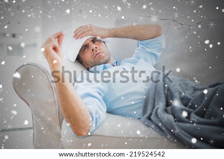 Composite image of sick man lying on sofa checking his temperature under a blanket against snow falling