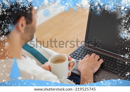 Brown haired man holding coffee using his laptop against snow