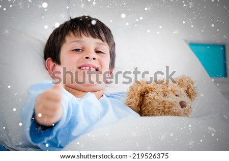Composite image of little boy hugging a teddy bear lying in a hospital bed against snow