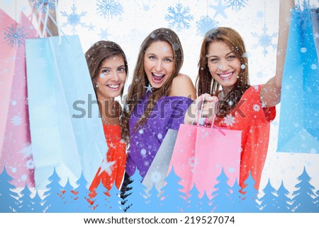 Three teenagers raising their arms while holding their purchases against snowflakes and fir trees in blue