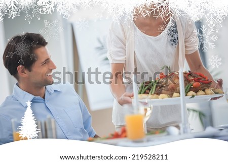 Smiling woman presenting a roast chicken during a dinner against fir tree forest and snowflakes
