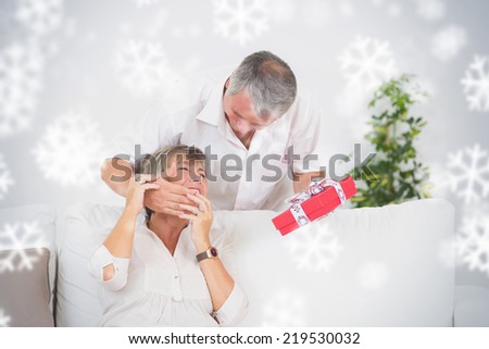 Composite image of Old man hiding eyes his wife to give a gift against snowflakes