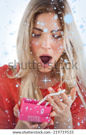 Composite image of Shocked woman discovering necklace in a gift box with snow falling