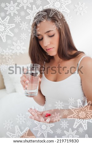 Woman looking down at the two pills she is going to take with water against snowflakes on silver