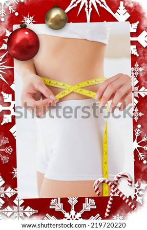 Toned woman measuring her waist against christmas themed page