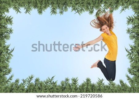 Pretty young woman jumping for joy against green fir branches
