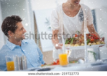 Smiling woman presenting a roast chicken during a dinner against snow falling