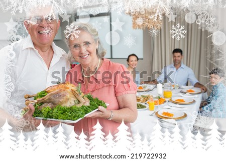 Grandparents holding chicken roast with family at dining table against fir tree forest and snowflakes